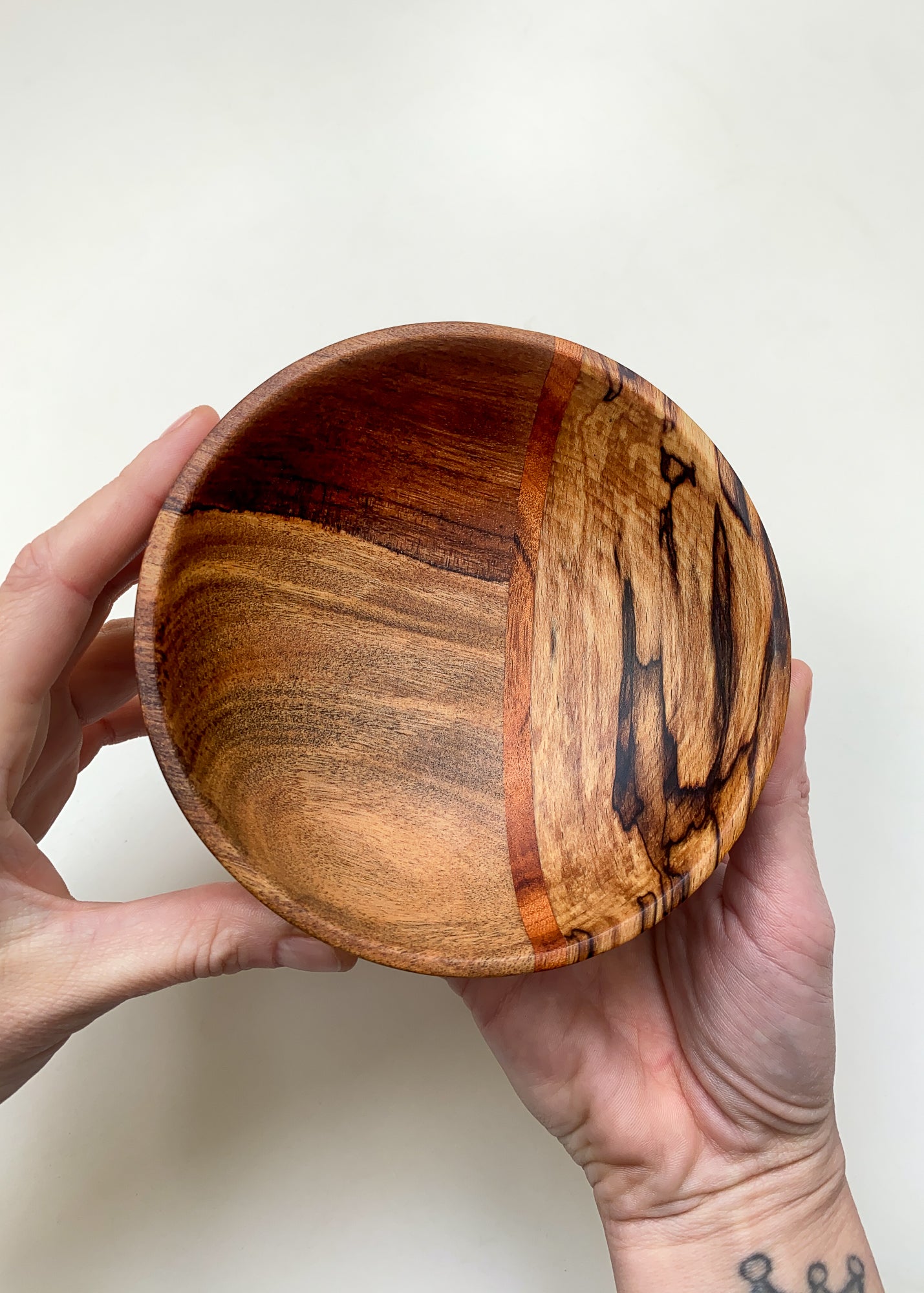 Small segmented wooden bowl held by a hand against a white background