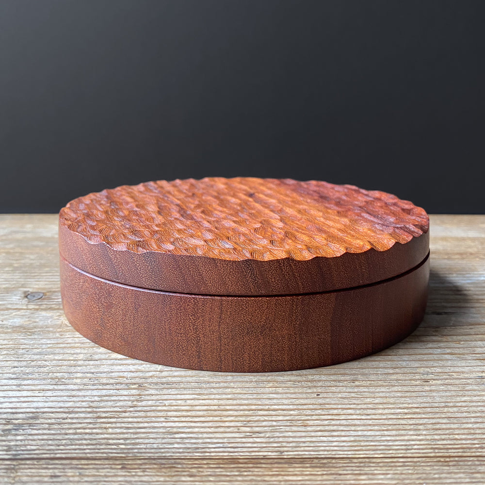 Shallow wooden box with a textured surface on a wooden table.