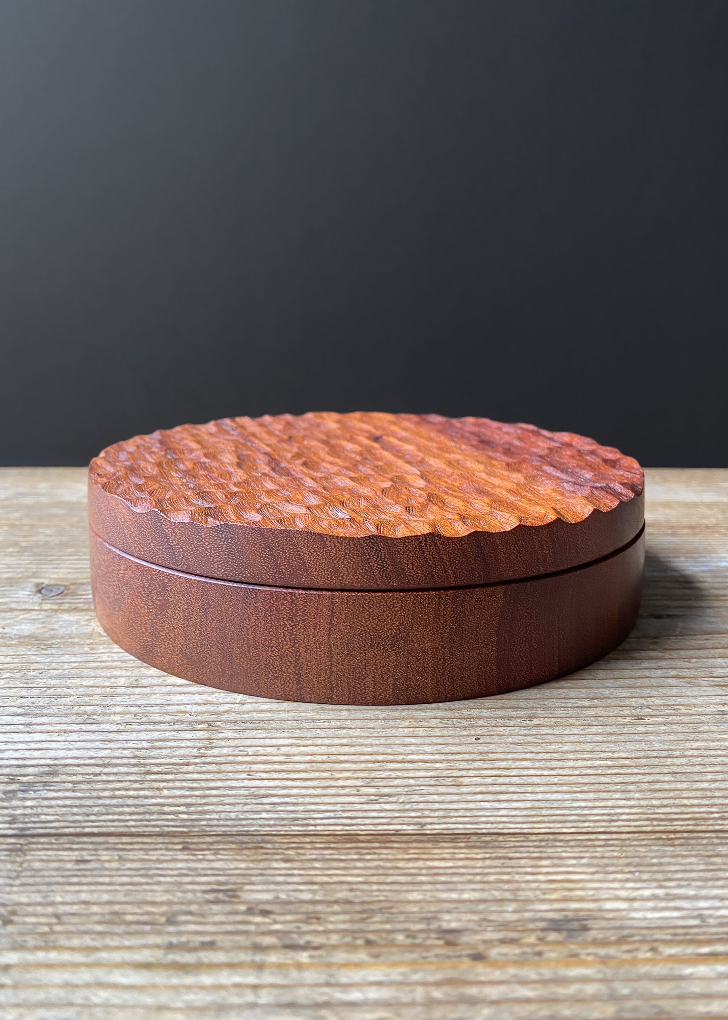 Shallow wooden box with a textured surface on a wooden table.