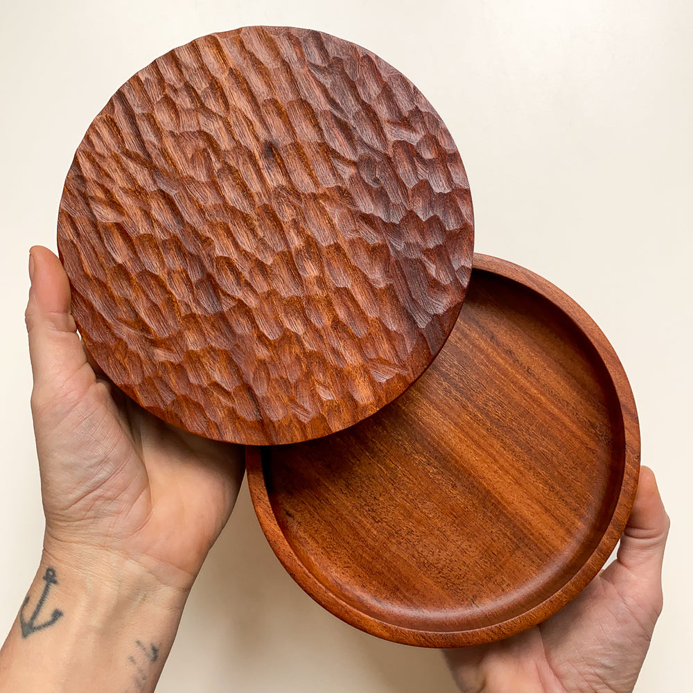 Shallow wooden box with textured lid held open in hands against white background.