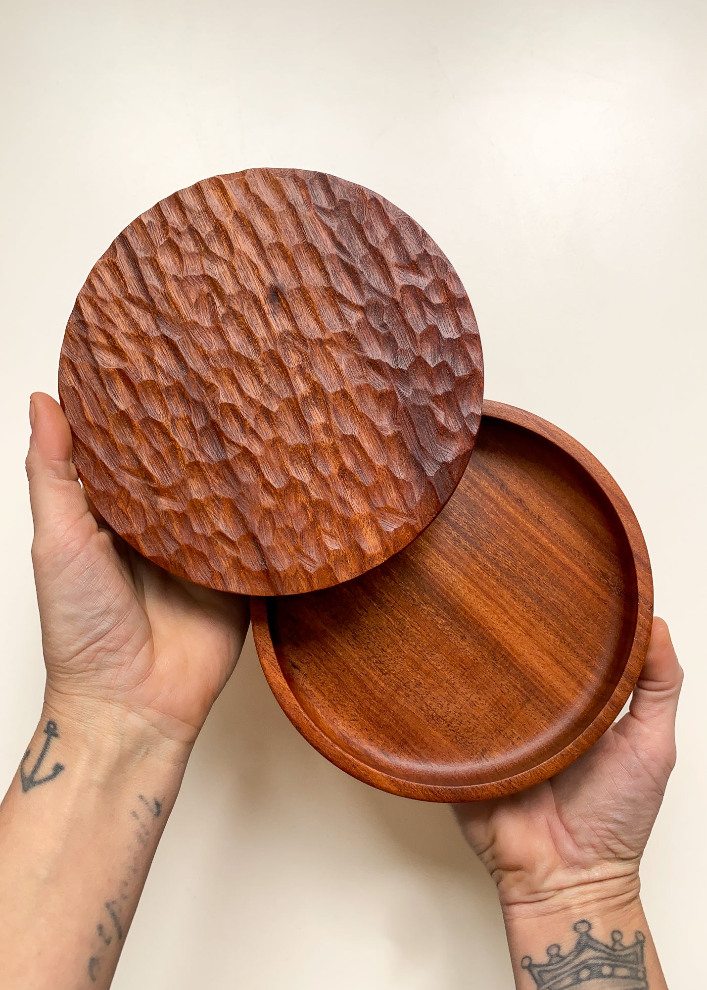 Shallow wooden box with textured lid held open in hands against white background.