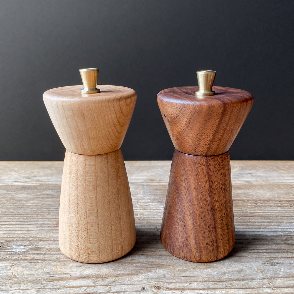 Two small wooden pepper mills on a wooden surface with a dark background