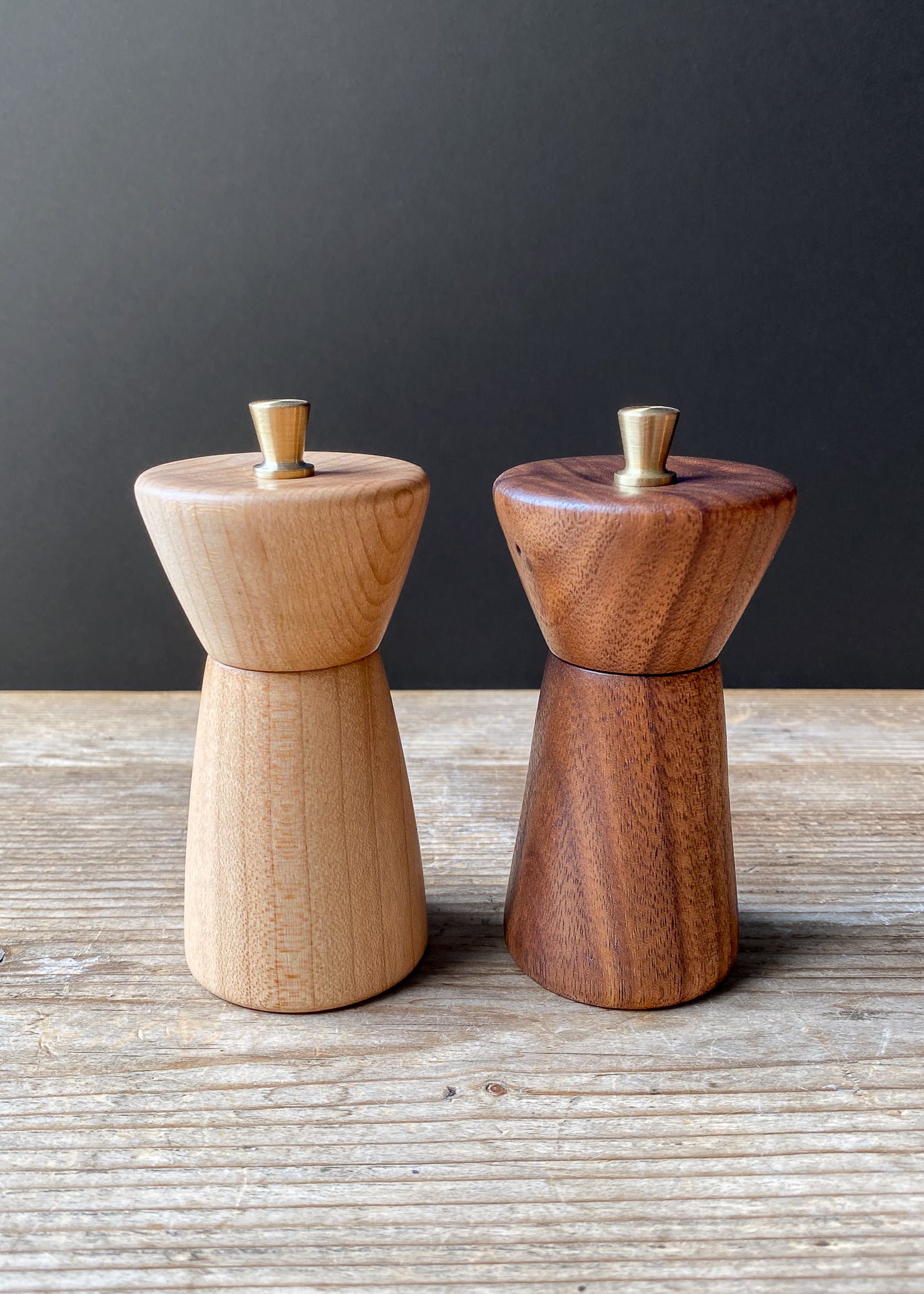 Two small wooden pepper mills on a wooden surface with a dark background