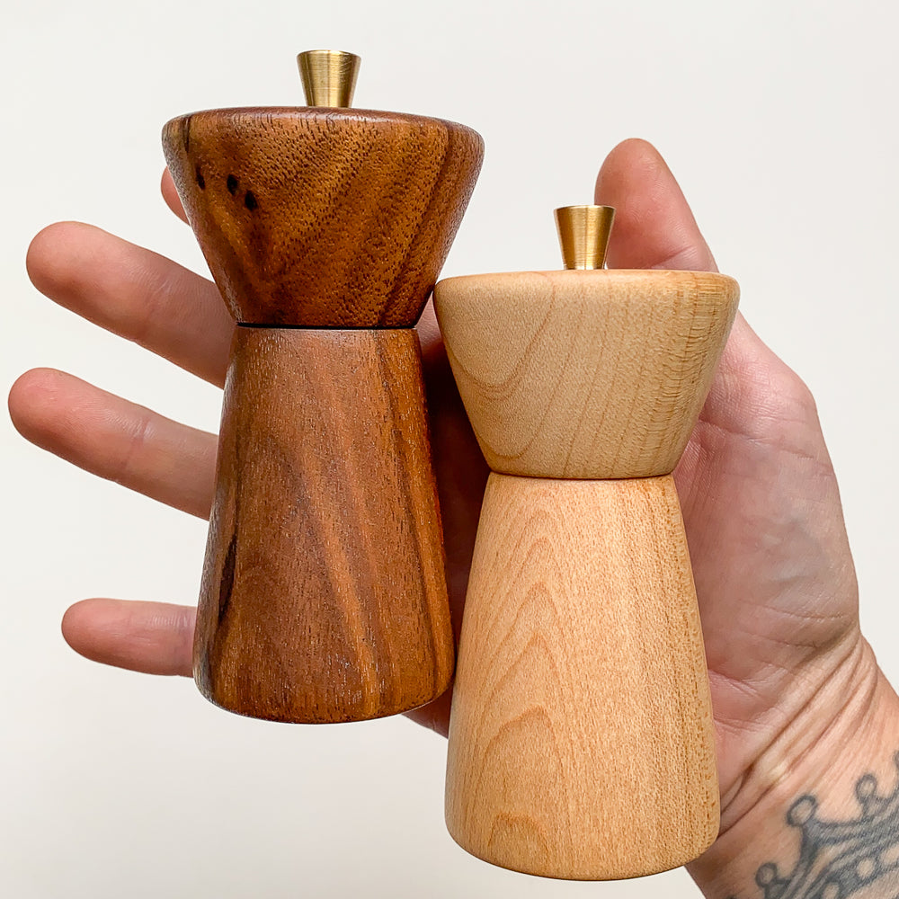 Hand holding two wooden pepper mills against a plain background
