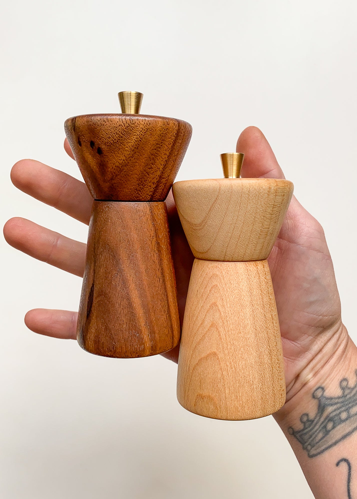 Hand holding two wooden pepper mills against a plain background