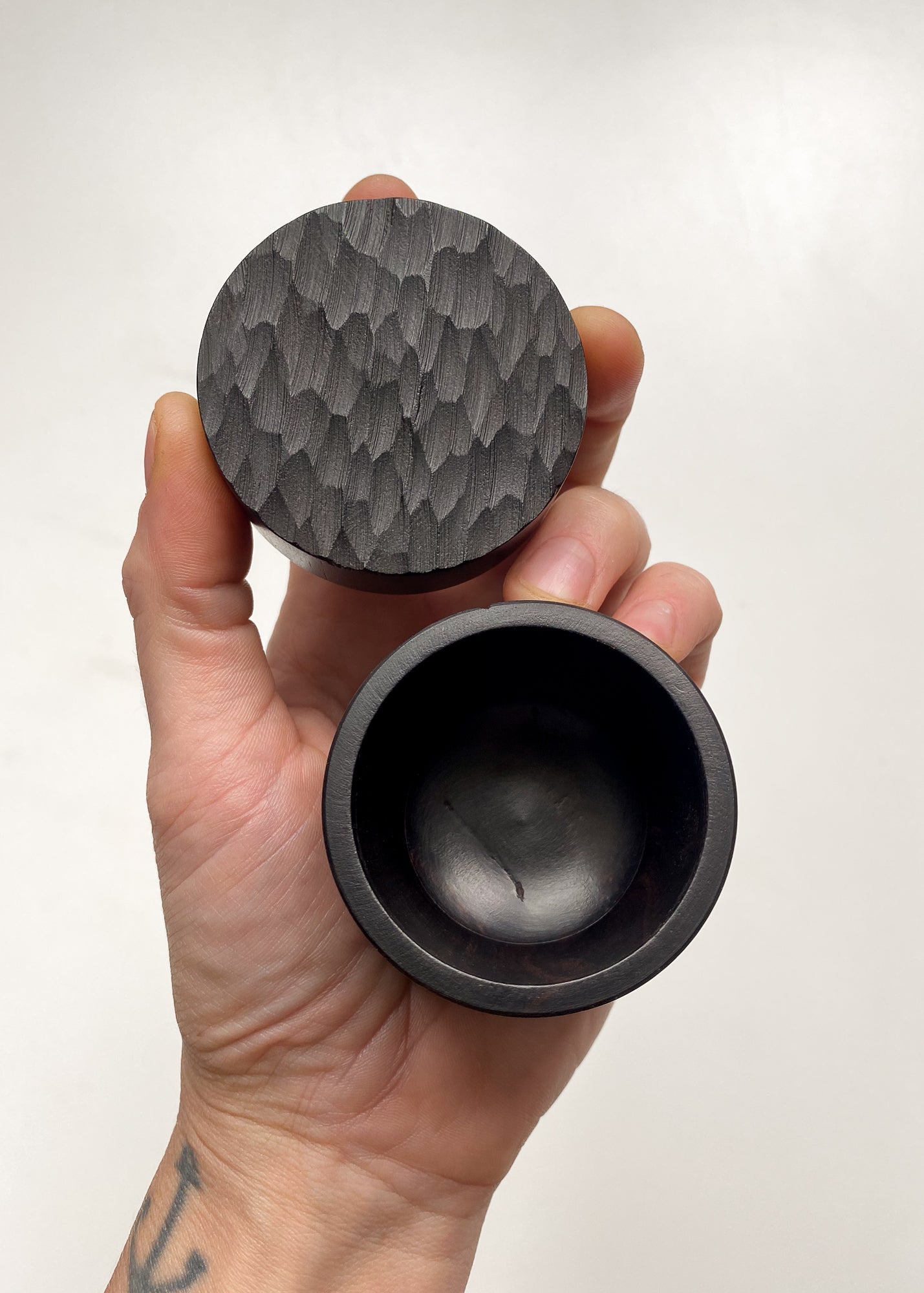 Hand holding opened small African Blackwood box with textured lid against white background.