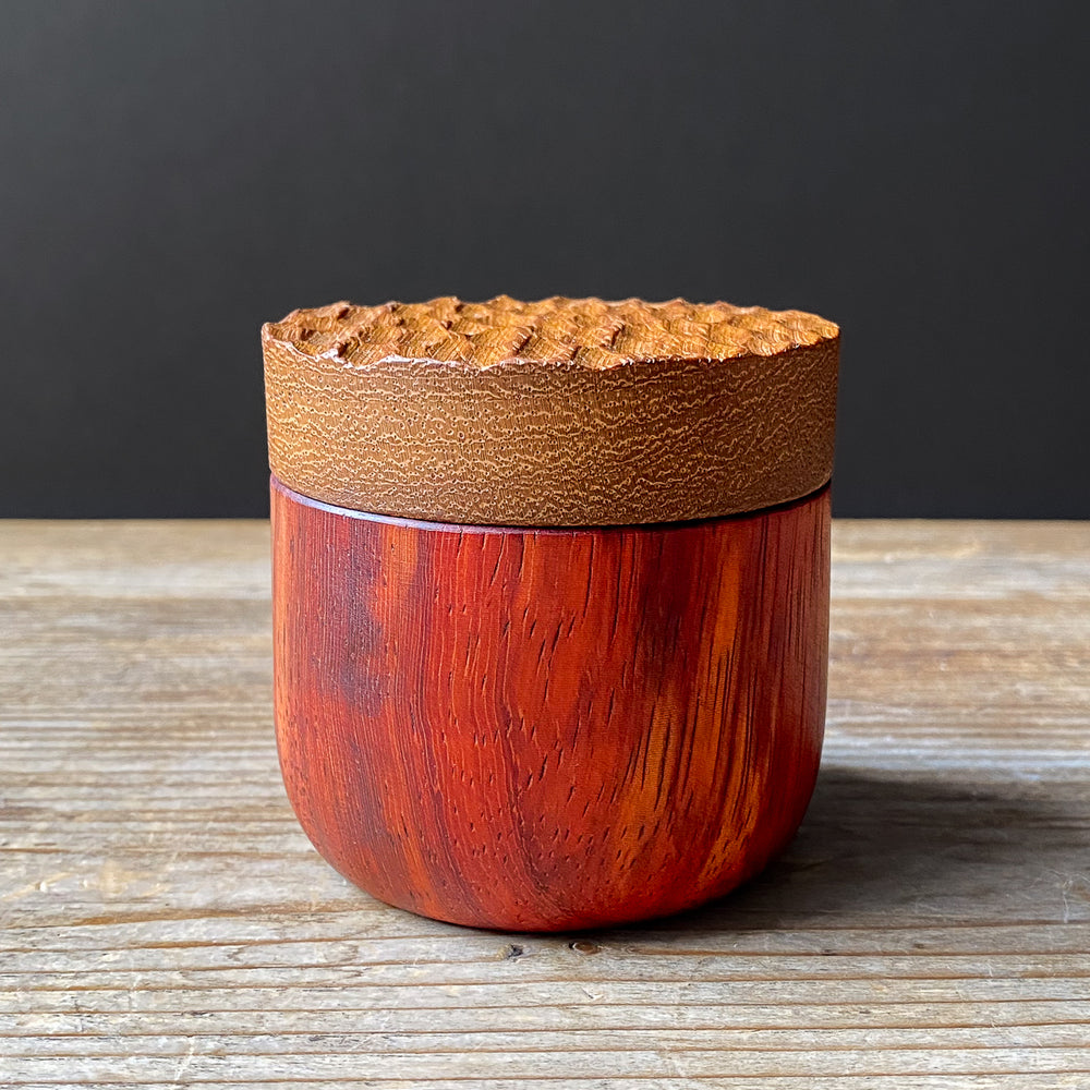 Two-toned wooden box with textured lid on wooden table against dark background.