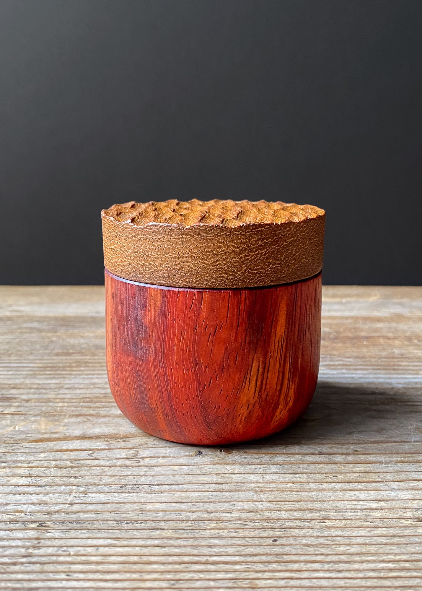 Two-toned wooden box with textured lid on wooden table against dark background.
