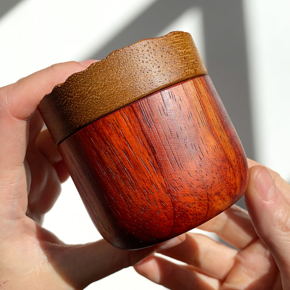 Side view of wooden box with red body and yellow lid held in hands against white background.