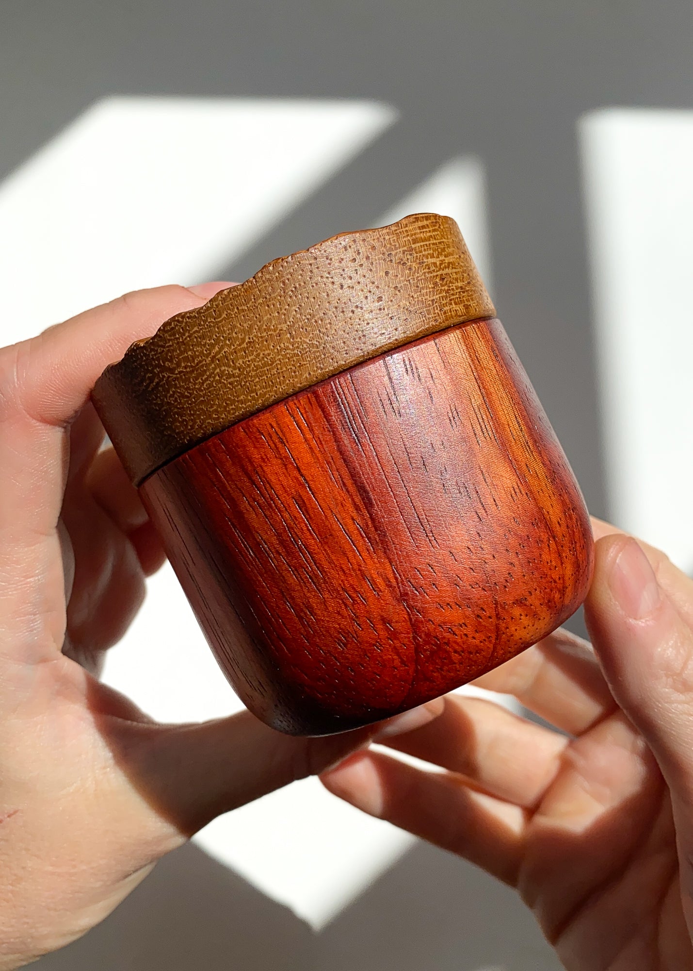 Side view of wooden box with red body and yellow lid held in hands against white background.