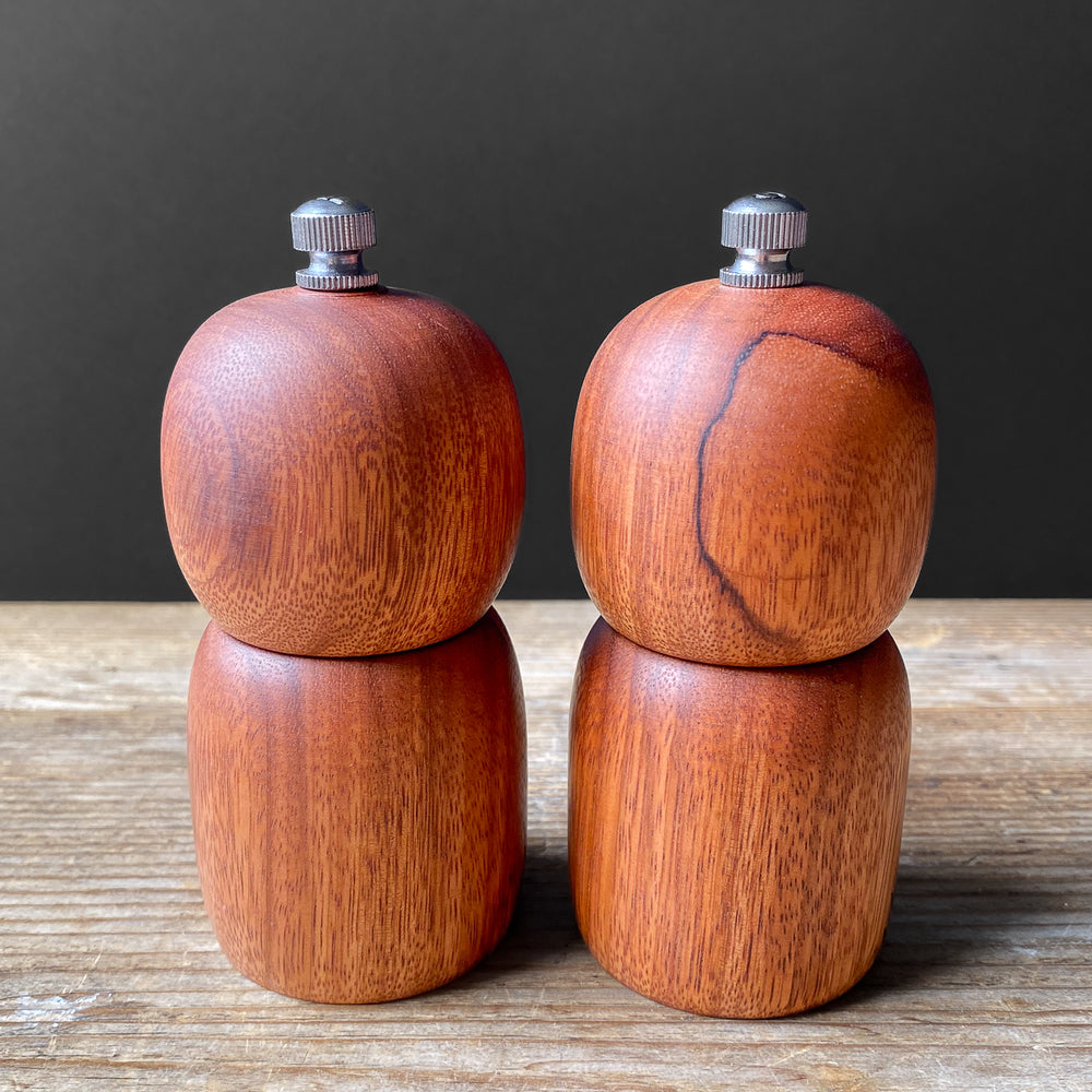 Set of small wooden salt and pepper mills on a wooden surface with a dark background