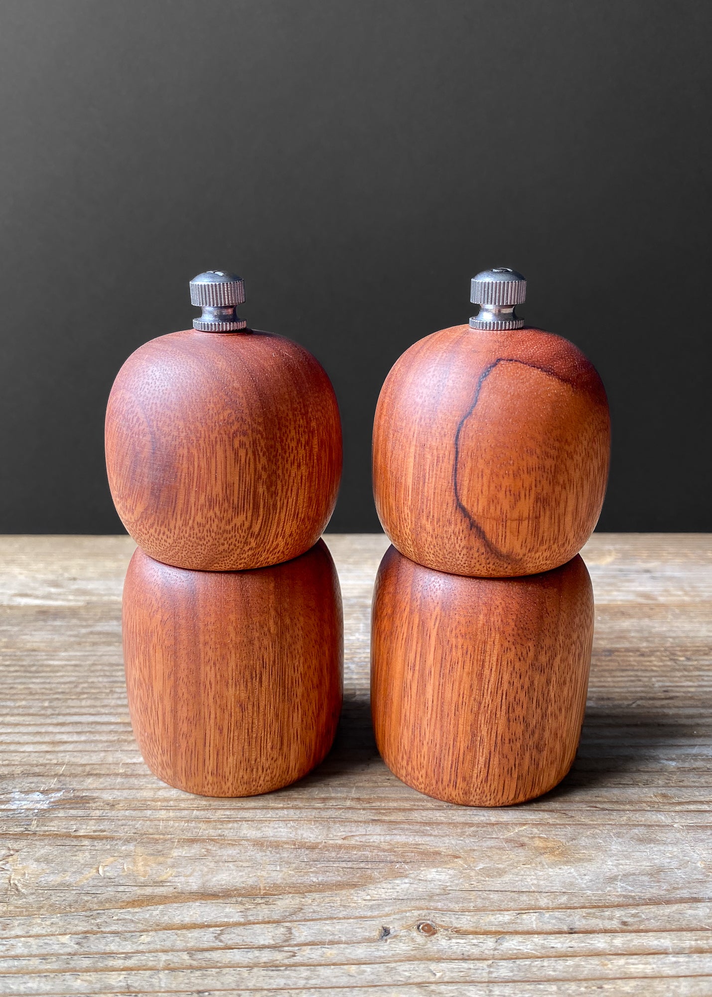 Set of small wooden salt and pepper mills on a wooden surface with a dark background