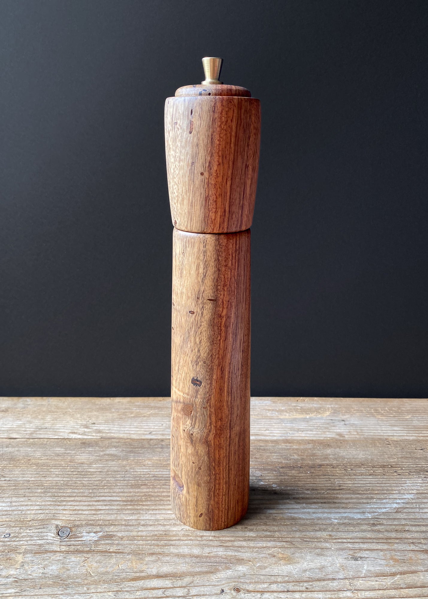 Wooden pepper grinder on a wooden surface with a dark background