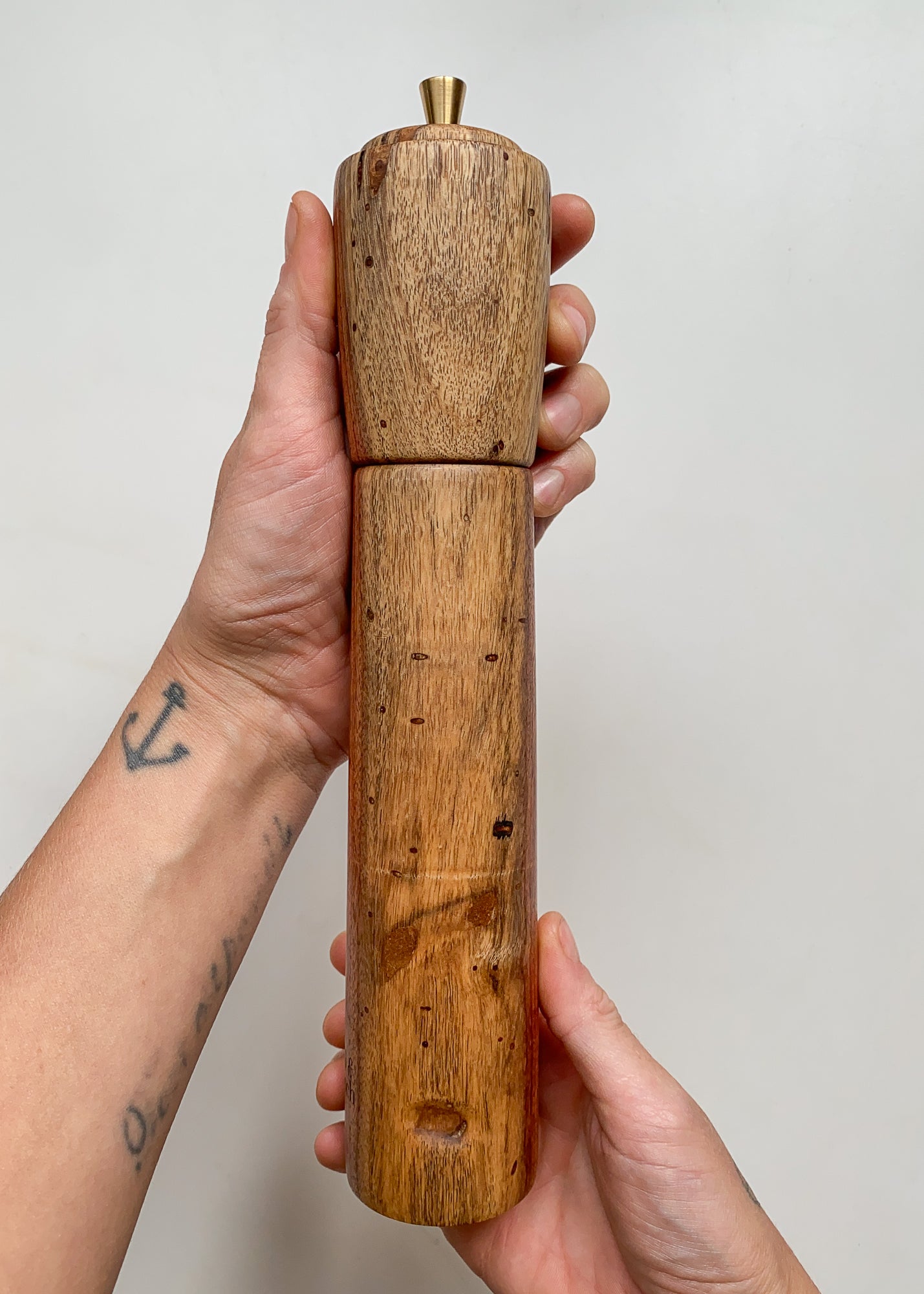 Large wooden pepper grinder with brass knobs held in hands against a plain background