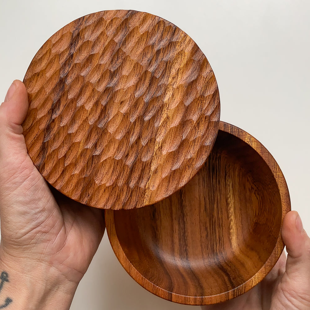 Overhead view of wooden box with textured lid held in hands against white background