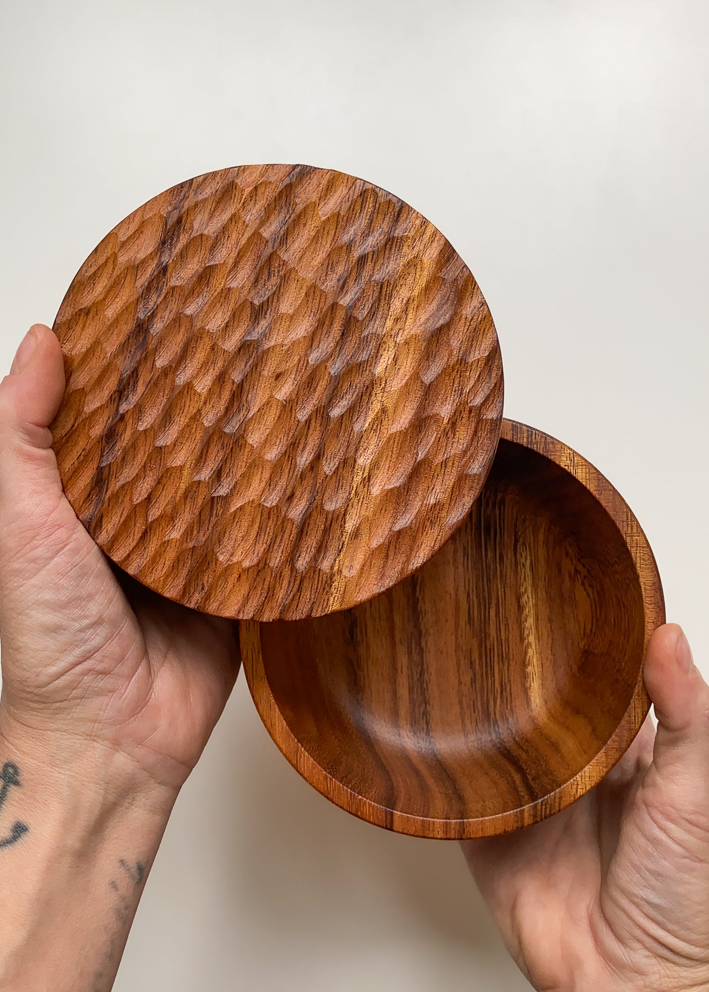 Overhead view of wooden box with textured lid held in hands against white background