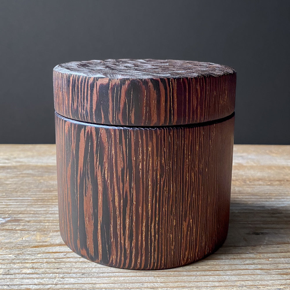 Wooden box with textured lid on a wooden surface against a dark background
