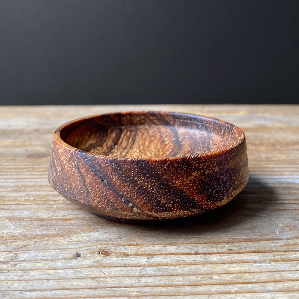 Wooden bowl with a striped pattern on a wooden surface with a dark background