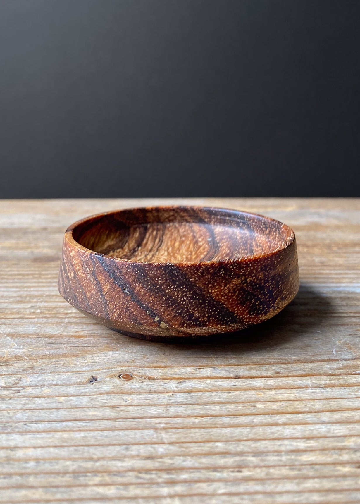 Wooden bowl with a striped pattern on a wooden surface with a dark background