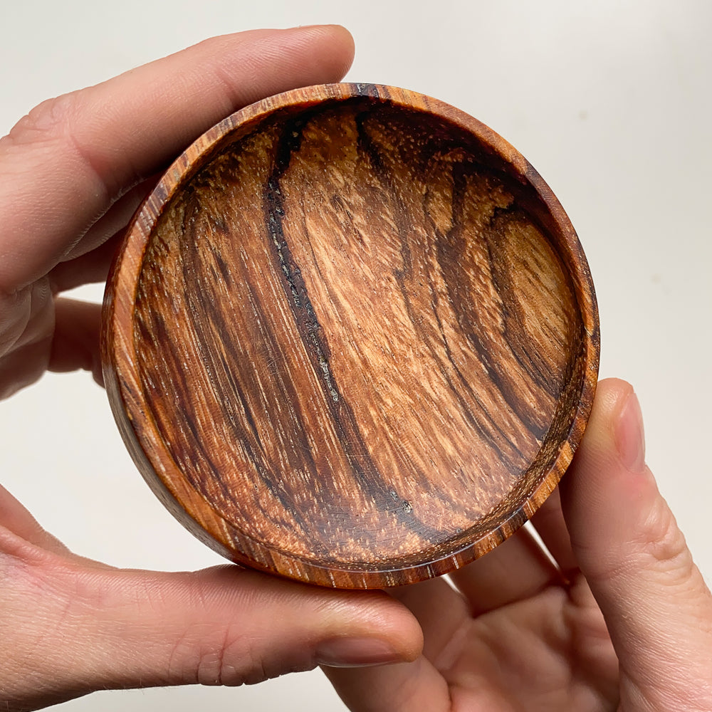 Striped wooden bowl held in hands against a neutral background