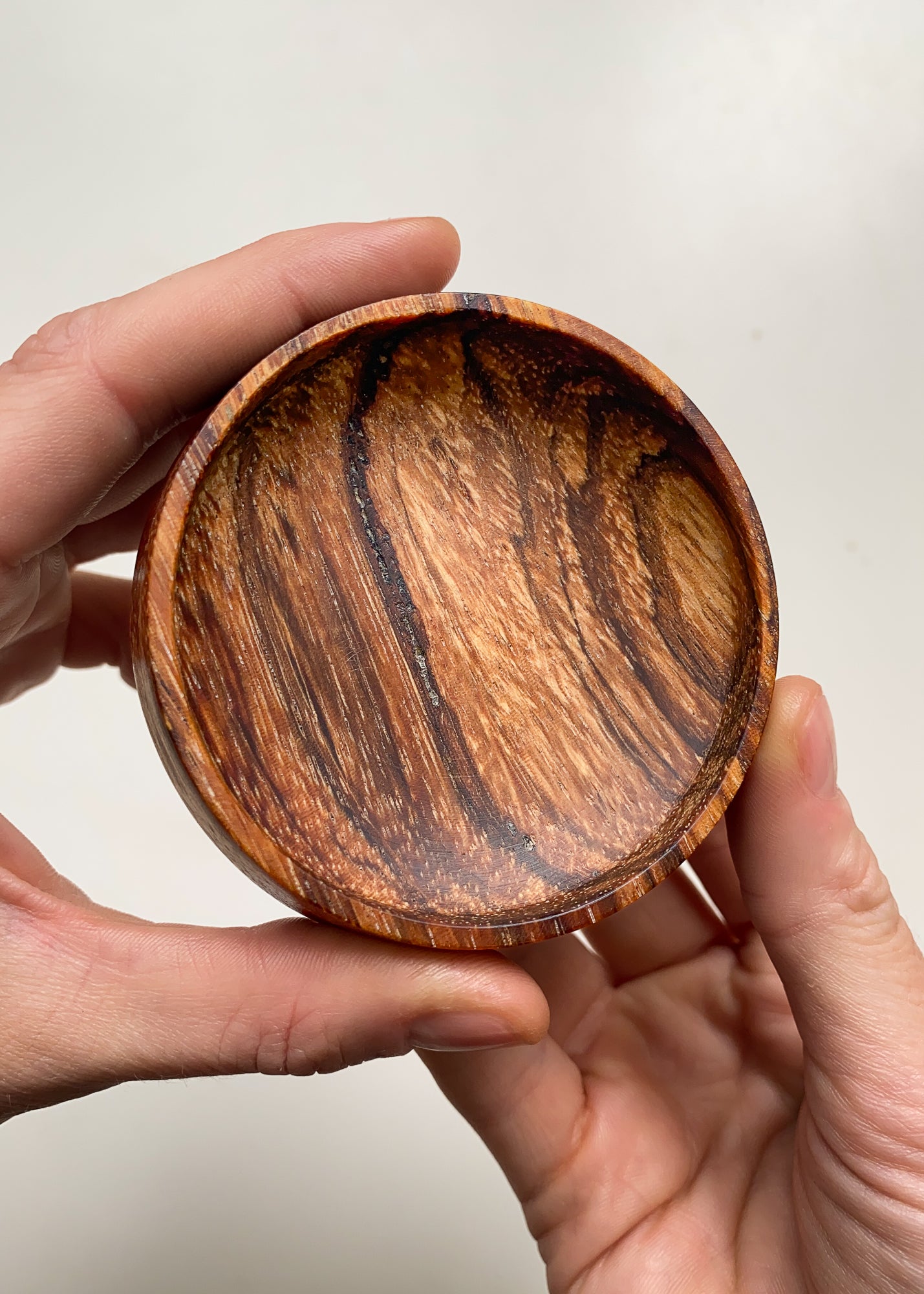 Striped wooden bowl held in hands against a neutral background