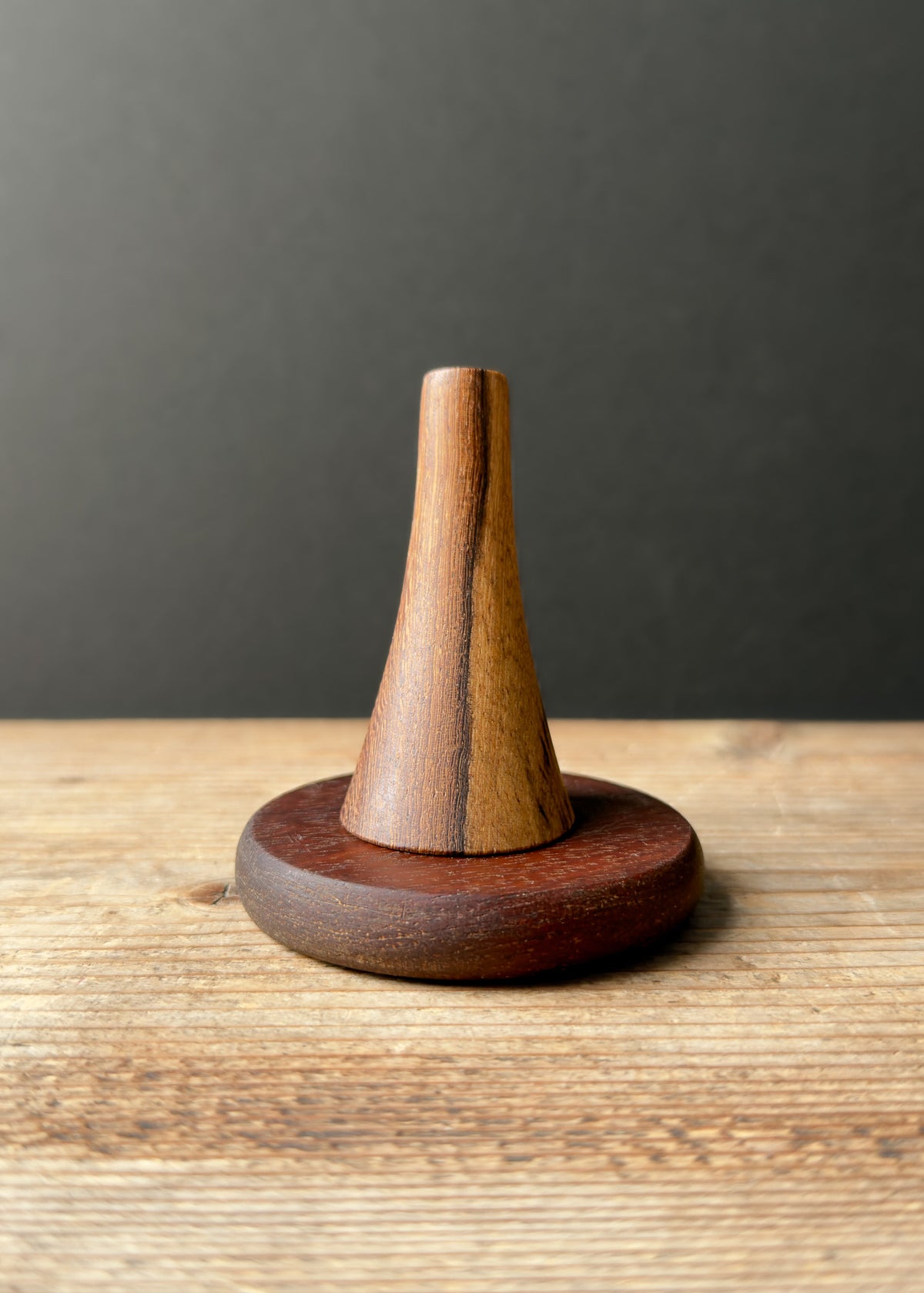 Wooden cone-shaped ring stand on a wooden base against a dark background