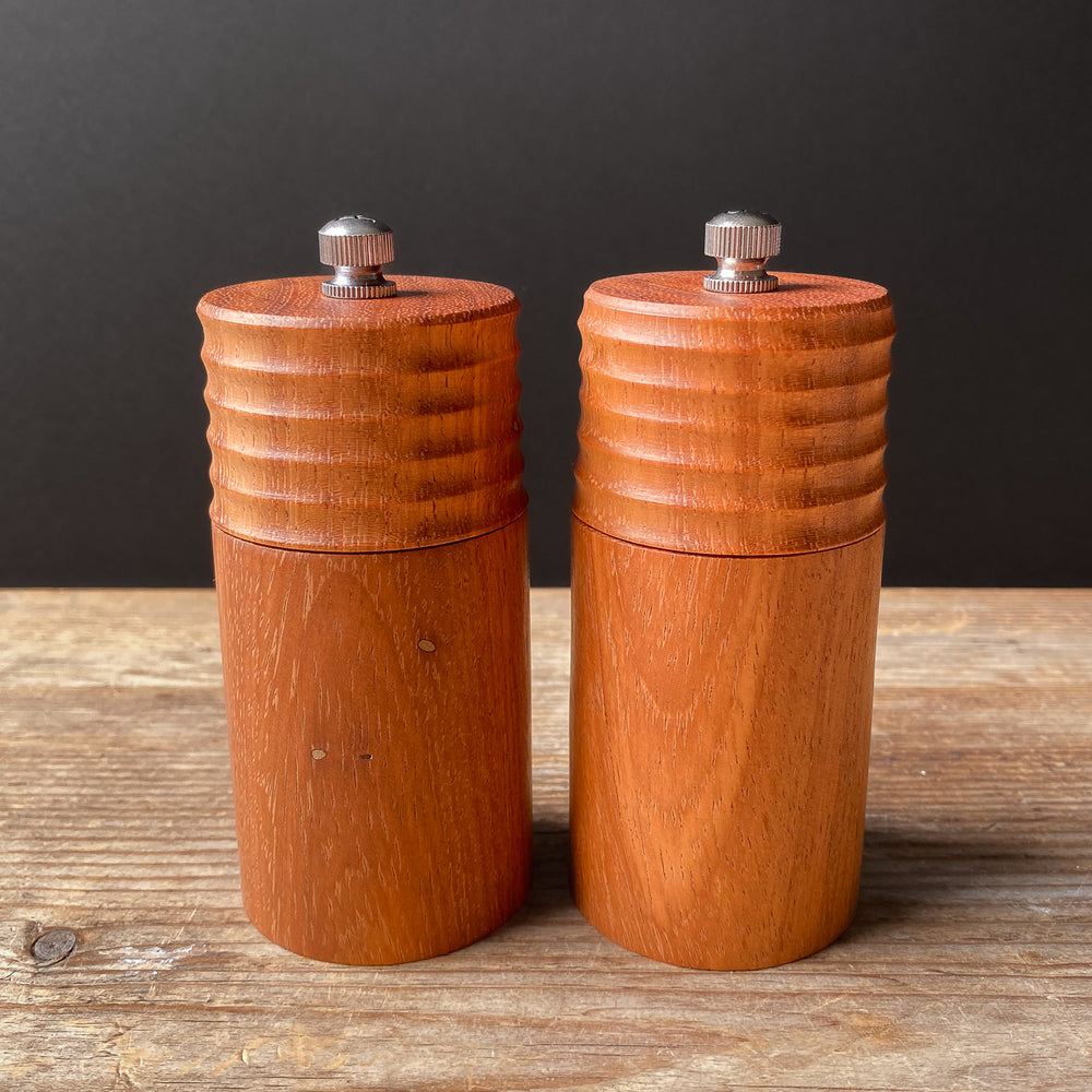 Two orange wooden pepper mills on a wooden surface with a dark background