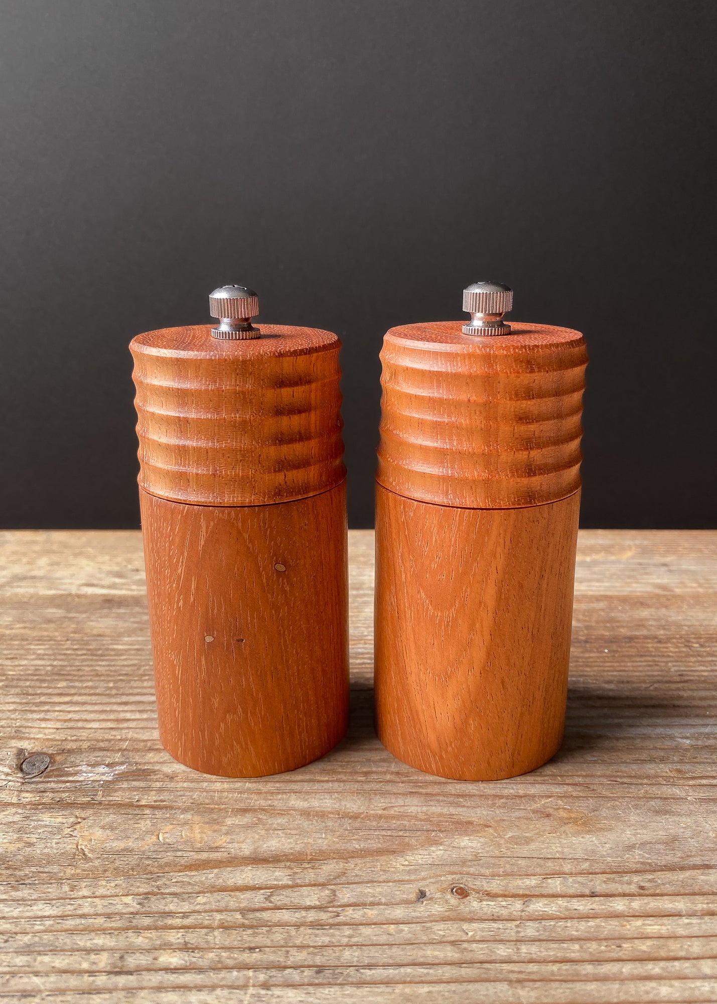 Two orange wooden pepper mills on a wooden surface with a dark background
