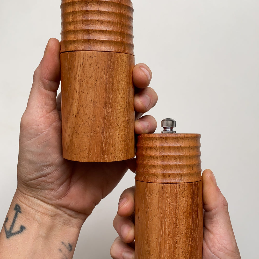 Two wooden pepper mills held in hands against a plain background