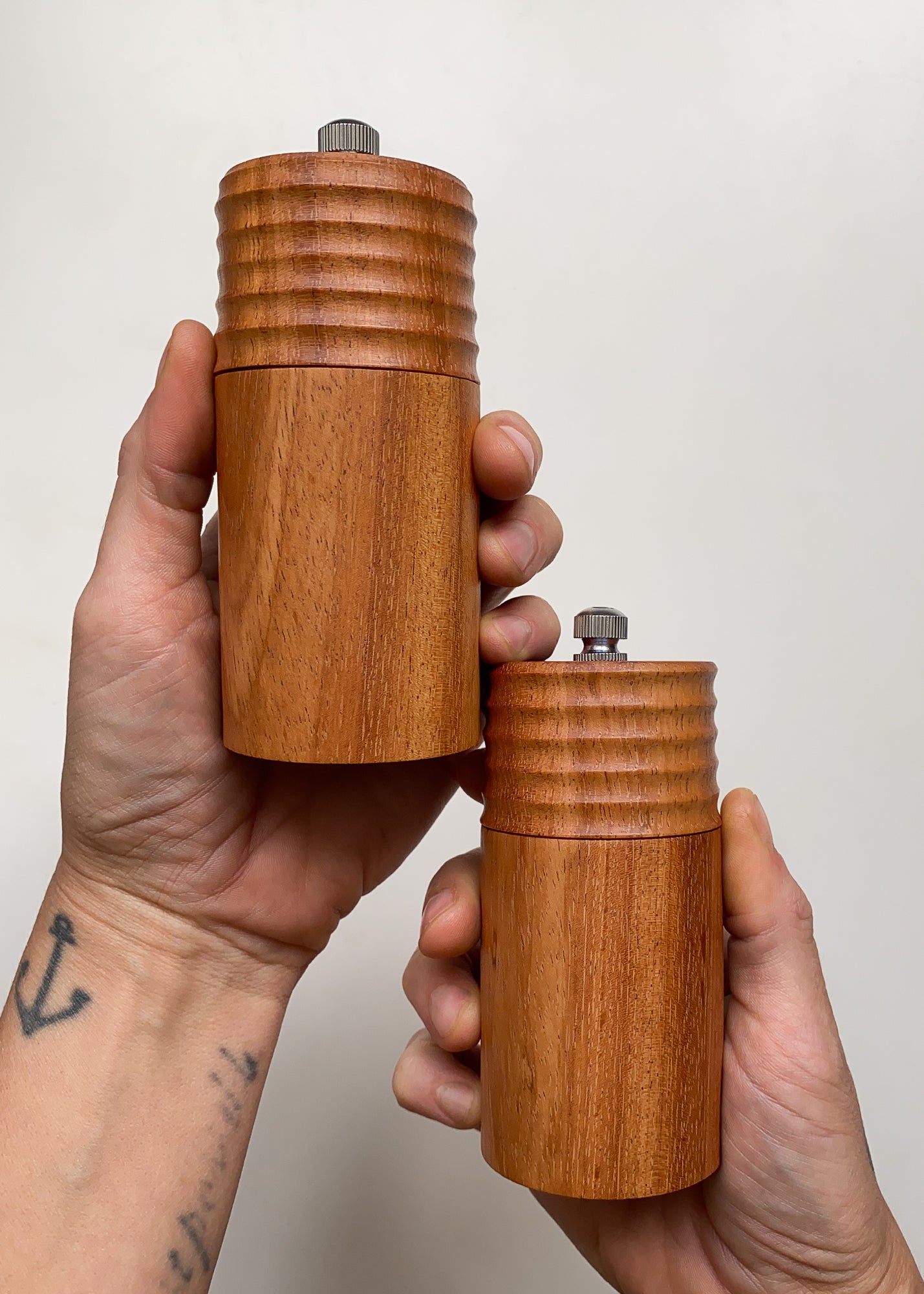 Two wooden pepper mills held in hands against a plain background