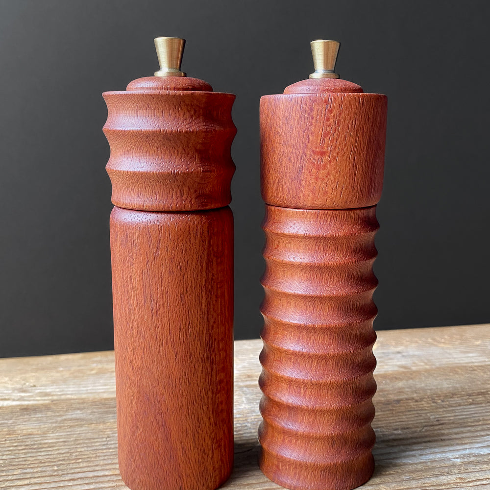 Two reddish brown wooden pepper mills on a wooden surface with a dark background