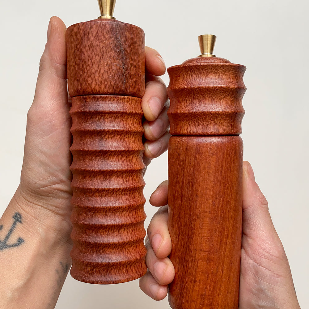 Two wooden pepper mills held in hands against a neutral background.