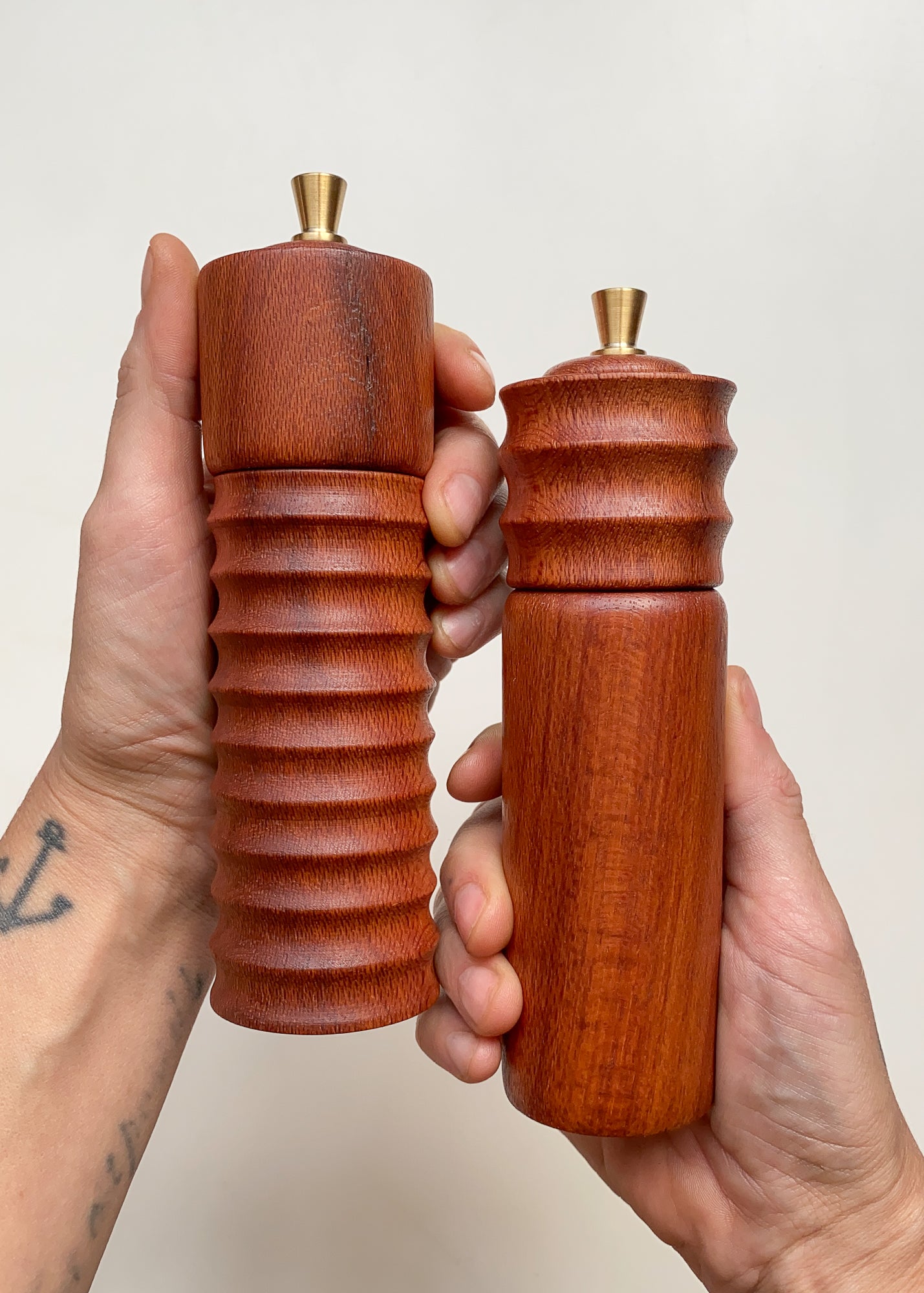 Two wooden pepper mills held in hands against a neutral background.
