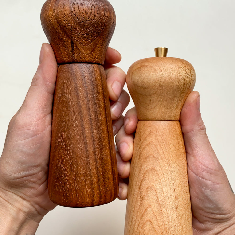 Two wooden pepper mills, held in hands against a plain background