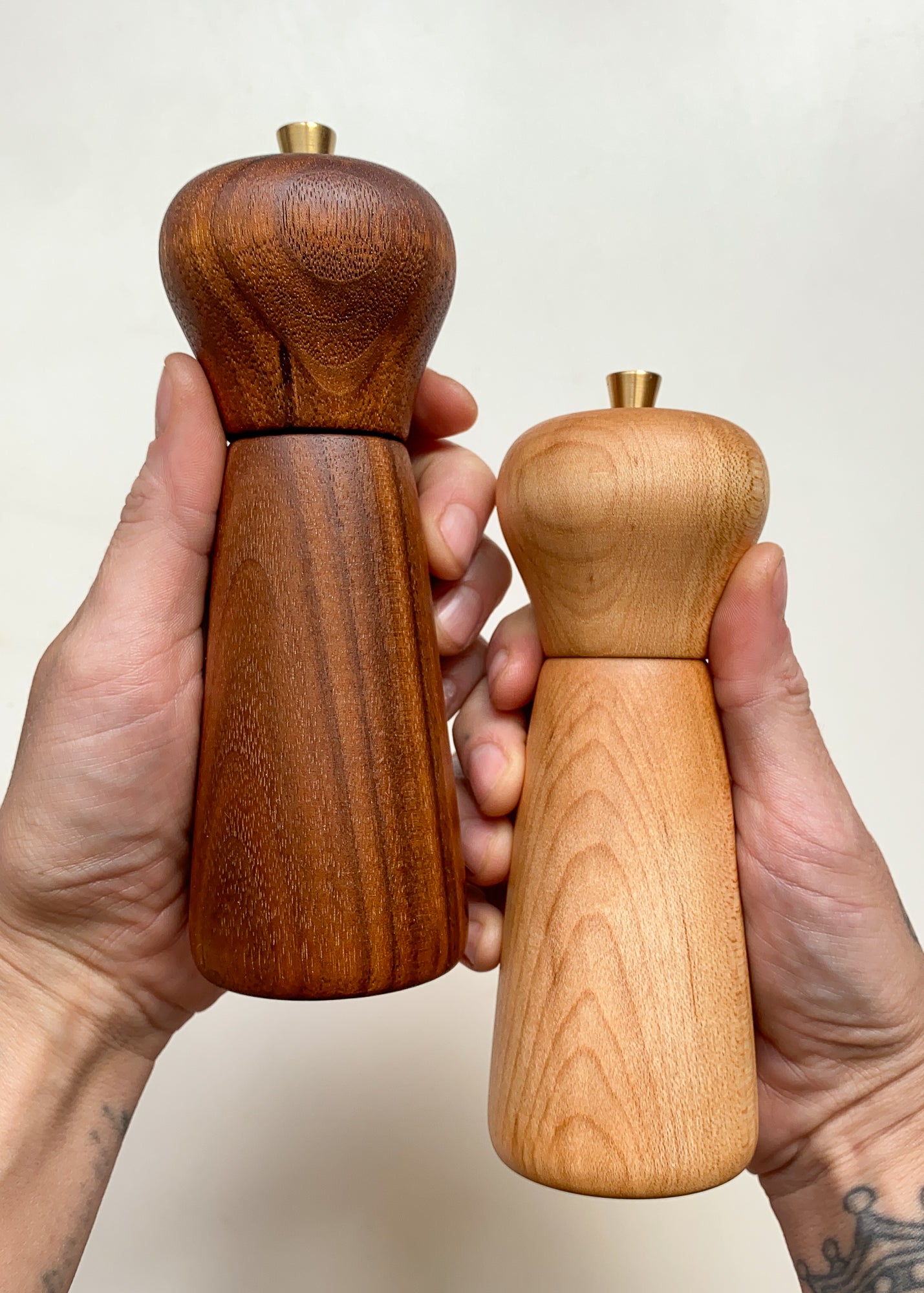 Two wooden pepper mills, held in hands against a plain background