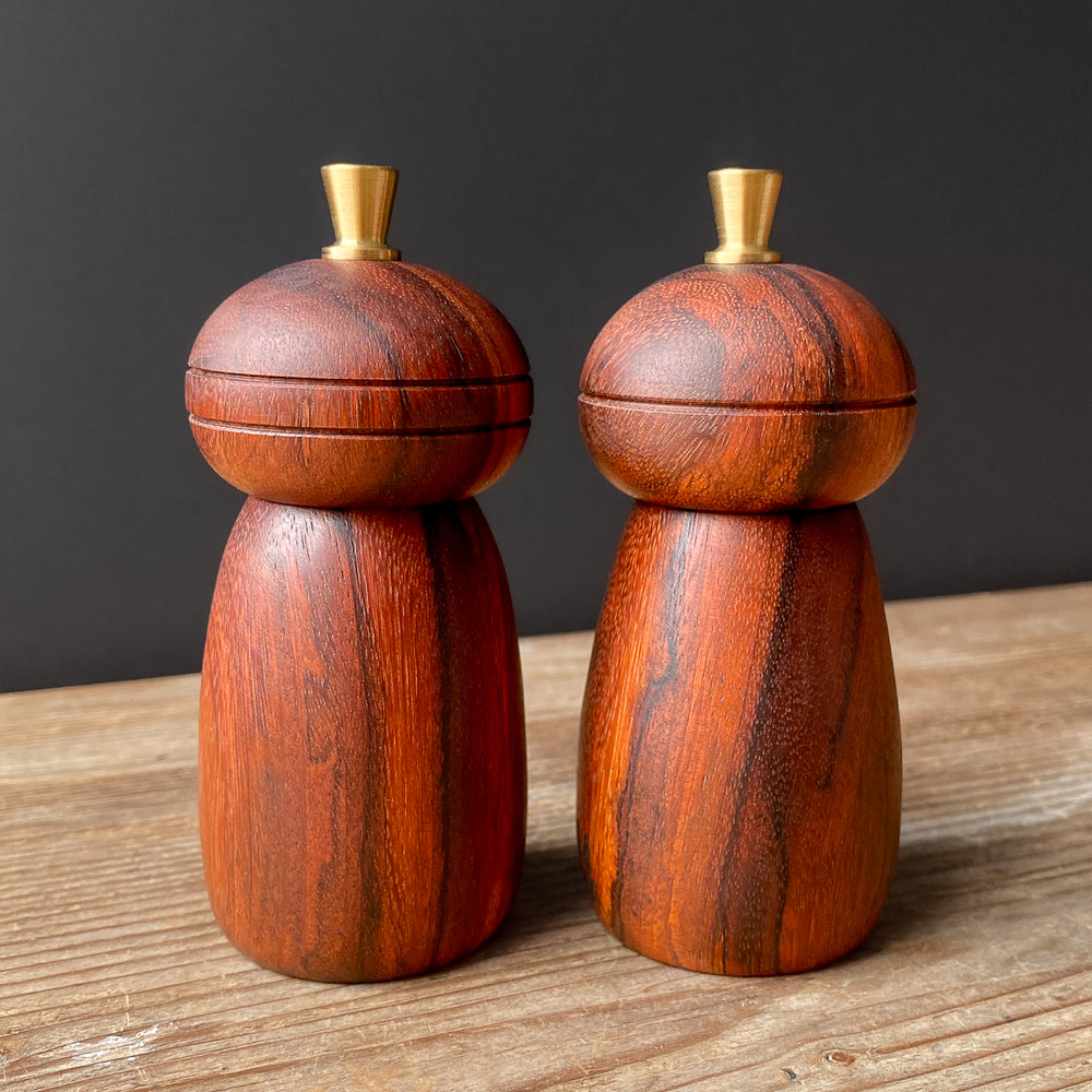 Two small wooden salt and pepper mills on a wooden surface with a dark background