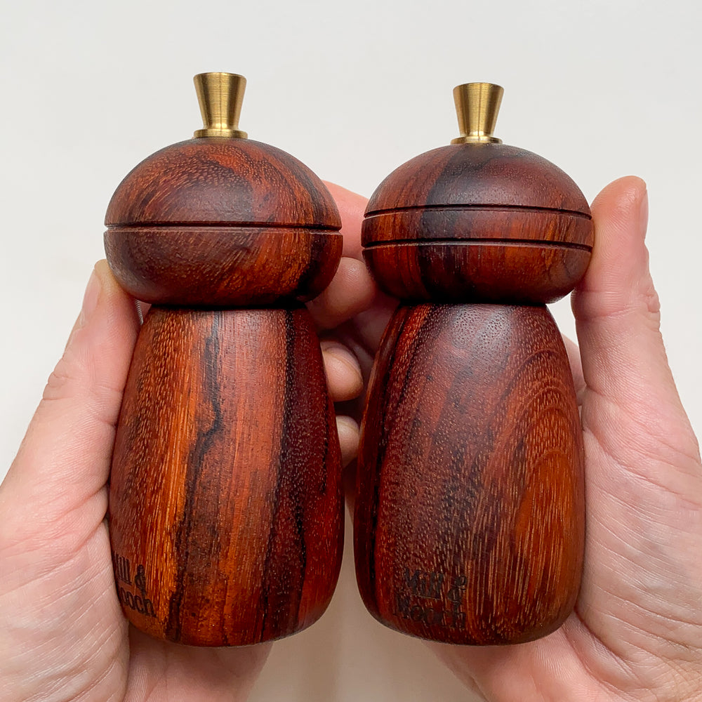 Two dark reddish brown salt and pepper mills held in hands against a plain background